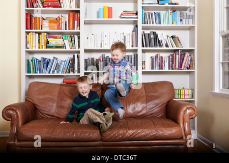 Two young brothers jumping on sofa Stock Photo