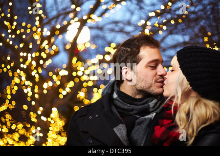 Young couple kissing in front of outdoor xmas lights Stock Photo