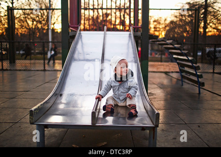 Baby boy sitting on slide in park