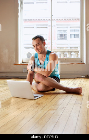 Mid adult man using laptop whilst in Cowface yoga pose Stock Photo