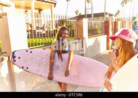 Two girls carrying surfboards laughing and smiling Stock Photo