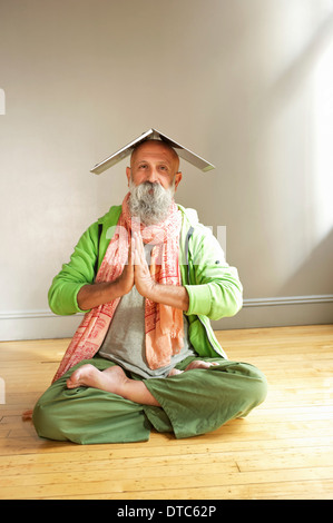 Senior man in lotus position with laptop on head Stock Photo