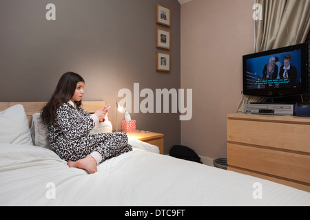 Teenage girl watches TV and texts on her mobile phone Stock Photo