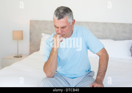 Pensive senior man sitting on bed Stock Photo