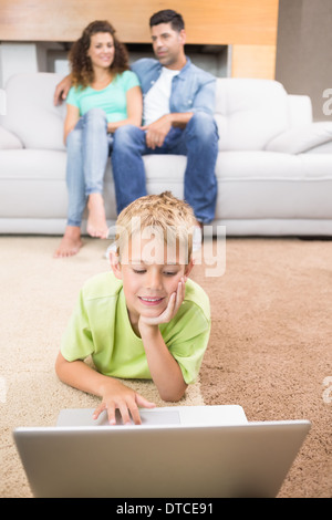 Cute little boy using laptop on the rug with parents sitting sofa Stock Photo