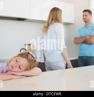 Girl leaning on table while parents arguing Stock Photo