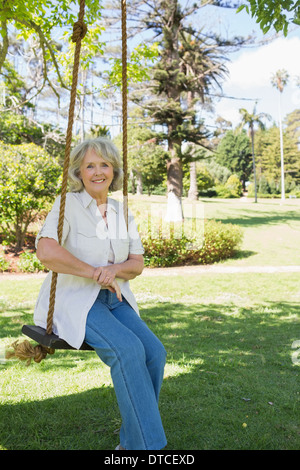 Smiling mature woman sitting on swing in park Stock Photo