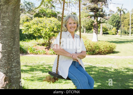 Smiling mature woman sitting on swing in park Stock Photo