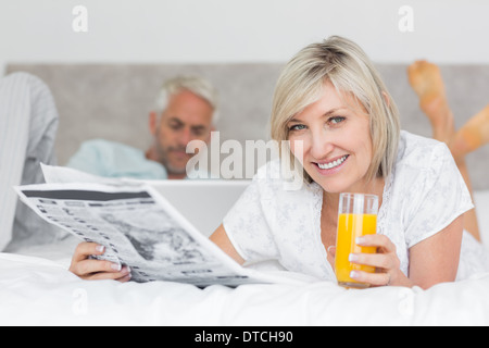 Couple reading newspaper and using laptop in bed Stock Photo