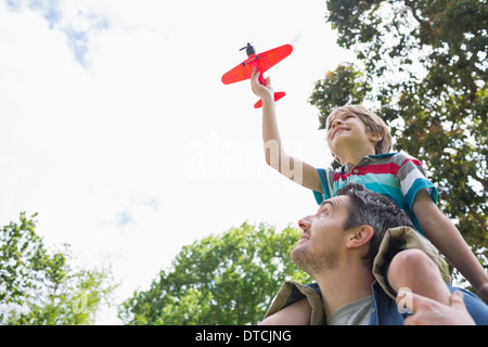Boy with toy aeroplane sitting on father's shoulders Stock Photo