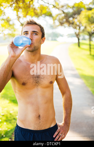 Athletic young man drinking water and relaxing after early morning workout, Running in the park. Stock Photo