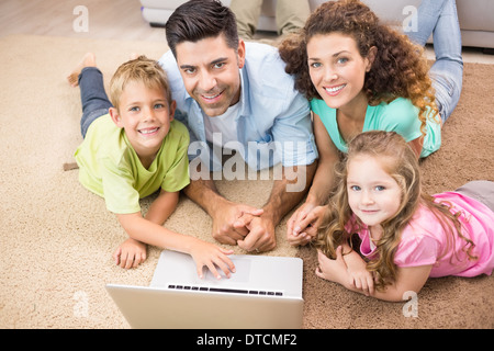 Happy siblings lying on the rug using laptop with their parents Stock Photo