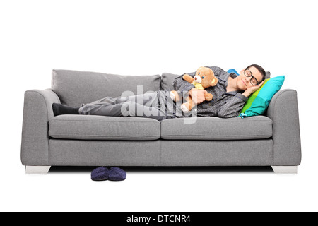 Young man in pajamas sleeping on couch with teddy bear Stock Photo