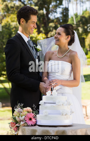 Newlywed couple cutting wedding cake at park Stock Photo