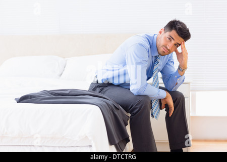 Frowning businessman sitting at edge of bed looking at camera Stock Photo