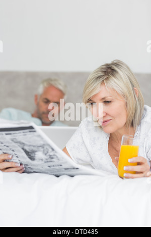 Couple reading newspaper and using laptop in bed Stock Photo