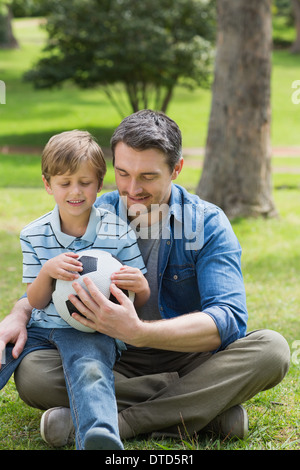 Father and son with football sitting on grass inpark Stock Photo - Alamy
