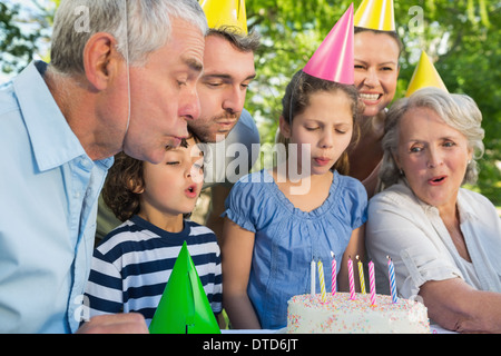 Extended family in party hats blowing birthday cake Stock Photo