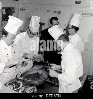 1960s and an historical picture showing of a group of male chefs in a kitchen preparing food for a banquet before cooking. Stock Photo