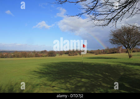 Epsom Downs, Surrey, England, UK. 15th February 2014. As more storms rage across the UK, a break in the clouds allows the sun to come out creating a rainbow over the flag of Epsom Downs Golf course. The skyline of London is just visible in the distance. Credit:  Julia Gavin/Alamy Live News Stock Photo
