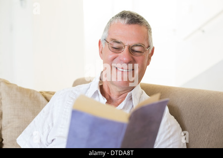 Senior man reading book on sofa Stock Photo