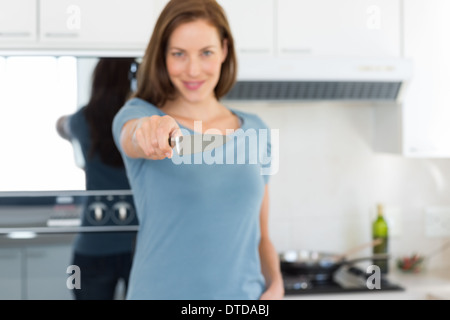 Smiling young woman holding out knife in kitchen Stock Photo