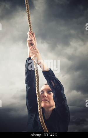 Woman climbing up with rope. Overcoming problems, obstacles and difficulties in life metaphor. Stock Photo