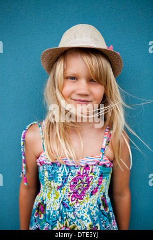 Portrait cute happy young girl wearing stylish hat outside against blue wall background Stock Photo