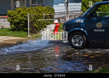 A damaged red fire hydrant spraying water on the city street and  municipal services vehicle close up front view nobody  horizontal in USA US hi-res Stock Photo