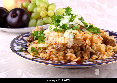 Uzbek pilaf in traditional dishes, fruits in background, horizontal Stock Photo