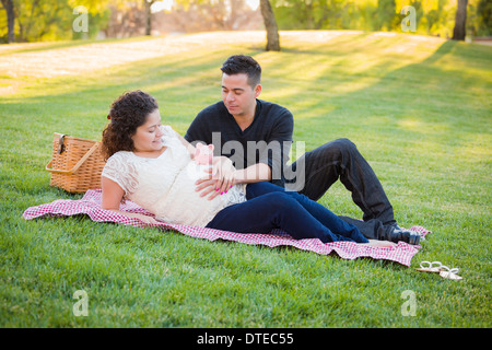 Contemplative Pregnant Hispanic Couple with Piggy Bank on Mother's Belly in the Park. Stock Photo