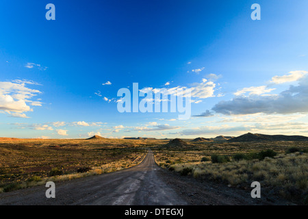 Empty,long blacktop road through miles of dry Namibian desert heading toward Kolmanskop on a bright sunny day. Stock Photo