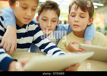 Three children sitting in cafe with touchpads Stock Photo