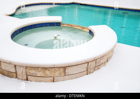 Outdoor hot tub or spa by swimming pool surrounded by snow in the winter Stock Photo