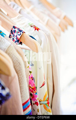 Light colored blouses with pops of color and floral motifs on wood hangers Stock Photo