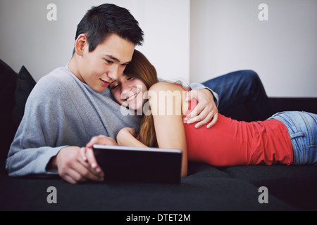 Teenage couple in love lying on sofa looking at tablet computer. Young asian couple watching movie on digital tablet. Stock Photo