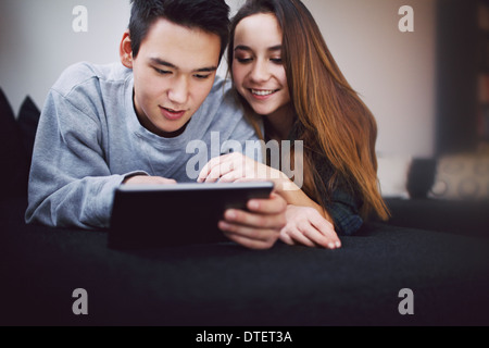 Relaxed teenage couple on lying together on sofa using digital tablet. Young asian man and woman on couch working on tablet. Stock Photo