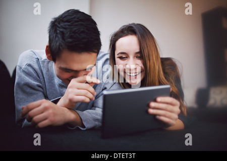 Happy young man and woman using tablet PC. Mixed race teenage couple using digital tablet smiling while lying on sofa at home.