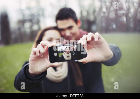 Cute young couple taking a self-portrait with a cell phone at the park. Mixed race teenage man and woman outdoors. Stock Photo