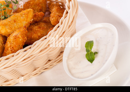 Crispy fried crumbed chicken nuggets in a wicker basket served as a finger food or appetizer with a creamy dip in a bowl alongside Stock Photo