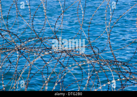 closeup of coiled razor-wire fencing patterns and textures against blue sea-water background Stock Photo