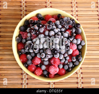 heap of frozen black currant and cherry covered with hoarfrost in the yellow plate Stock Photo