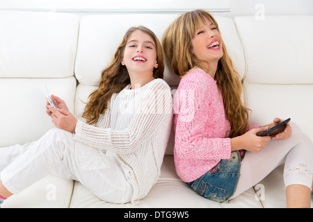 Children friends kid girls having fun playing back to back with tablet pc on white sofa Stock Photo