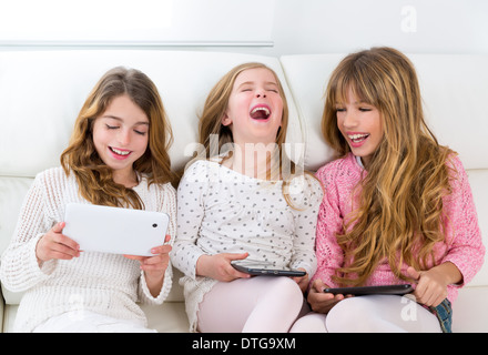 three kid sister friends girls group playing together with tablet pc on white sofa Stock Photo