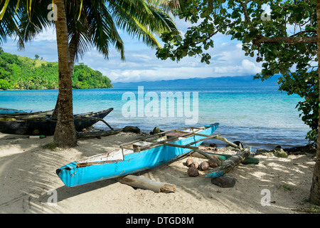 A blue Polynesian outrigger that's still used today rests on the shore of a tropical island in Fiji Stock Photo