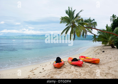Three orange kayaks sit on a resort beach on an exotic island in Fiji. Stock Photo