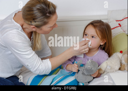 Mother taking care of her sick daughter, wiping the girl's nose, girl lying in bed Stock Photo