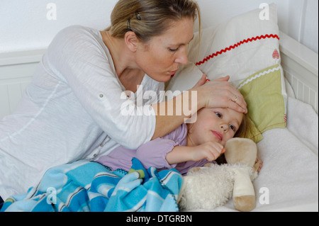 Mother taking care of her sick daughter, child lying in bed Stock Photo