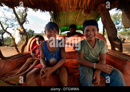 Indigenous children sitting on an old sofa in the shade, in the village of the Xavantes people, Tres Rios near the mission of Stock Photo