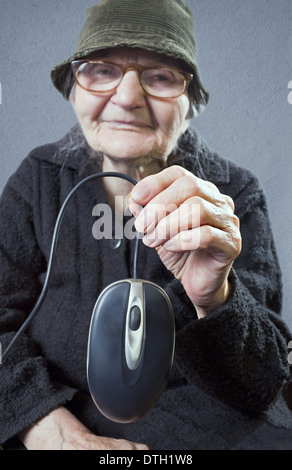 Elderly woman holding up a computer mouse. Selective focus om computer mouse. Stock Photo